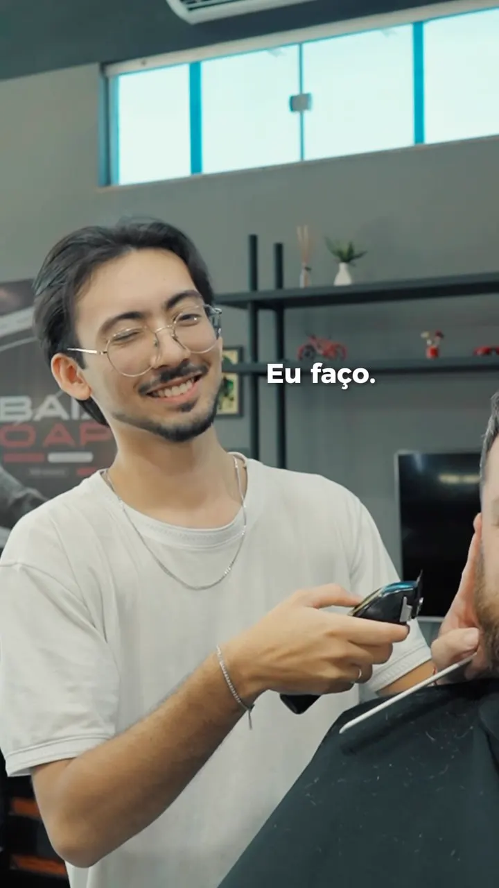 Barbeiro sorrindo com a máquina na mão durante o acabamento da barba